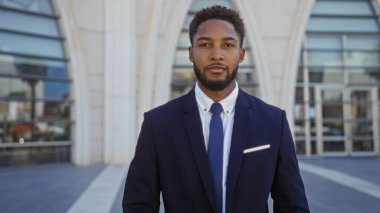 Şehrin modern mimarisinin önünde takım elbiseli ve kravatlı bir genç güvenli bir şekilde dışarıda duruyor.