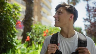 Parlak çiçekler ve yeşilliklerle dolu bir parkta gezinen genç adam, gülümsüyor ve mutlu görünüyor.