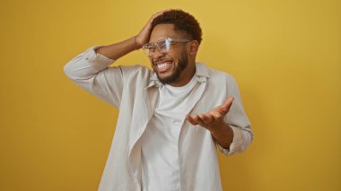 İzole edilmiş sarı arka planda gülümseyen genç adam neşeli bir ifadeyle, gözlük takıyor ve günlük kıyafetler giyiyor, canlı duygular ve enerji sergiliyor.