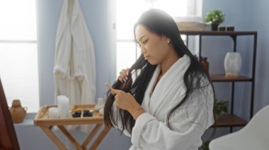 Beyaz bir bornoz giymiş, uzun saçlarını düşünceli bir ifadeyle tarayan bir kadın mavi duvarları ve çeşitli sağlık malzemeleriyle dolu sakin bir spa odasında..