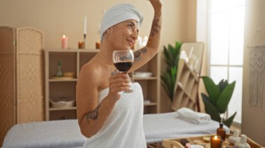 Olgun bir kadın güzel dekore edilmiş bir sağlık merkezinde elinde şarap kadehiyle rahatlatıcı spa gününün tadını çıkarıyor.