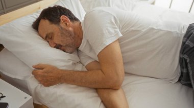 İspanyol bir adam yatakta uyuyor, olgun, yaşlı birini gösteriyor. Beyaz yastıklı ve huzurlu bir atmosferi olan bir yatak odasında rahatça dinleniyor..