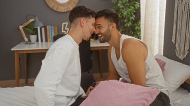 Erkekler sıcak bir yatak odasında sevgi gösteriyorlar, bir yatakta birlikte oturuyorlar ve neşeli bir anı paylaşıyorlar. Parlak ve davetkar bir iç mekanda.
