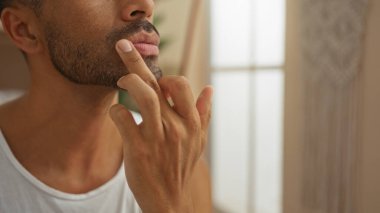 Genç bir adam huzur dolu bir spa odasında dudak kremi sürüyor. Güzellik merkezinde yaşayan yakışıklı bir İspanyol 'un huzur dolu sağlık ortamını ve kişisel bakım rutinini vurguluyor..