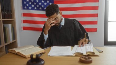 Yargıç, arka planda Amerikan bayrağı olan belgeleri mahkeme salonunda inceliyor..