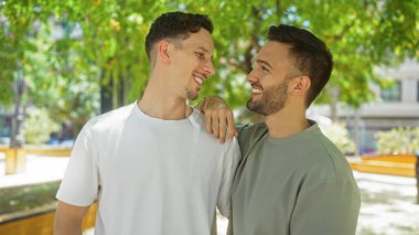 Gündüz vakti şehir parkında birlikte gülümseyen eşcinsel çift. Çevrelerinde yeşillik, aşkı ve mutluluğu simgeliyor..