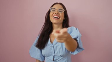 Çekici genç İspanyol kadın pembe bir arka planda tek başına dikilirken gülüp işaret ediyor..