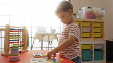 Küçük çocuk parlak bir anaokulu ortamında eğitici oyuncaklarla oynuyor, eğitici, eğlenceli ve ilgi çekici bir ortamda çocukluk boyunca şekilleri ve renkleri keşfediyor.