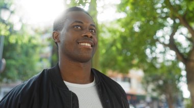 Şehir parkında kendine güvenen genç bir adam güneşli bir günde çevrenin yeşil ağaçlarla çevrili olması açık havada hayat ve iyimserliğin esansını yakalıyor.