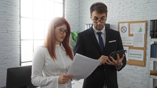Деловые партнеры обсуждают документы в офисе с мужчиной с помощью планшета и женщины, держащей бумаги, демонстрируя условия совместной работы в помещении.