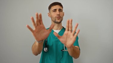 Young hispanic male doctor makes stop gesture with hands in front of isolated white background, exuding confidence and determination in a professional setting. clipart