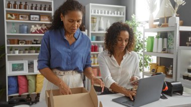 Kadınlar, arka planda çeşitli eşyalarla dolu rafları olan bir ev dekorasyonu mağazasında sipariş paketliyorlar.