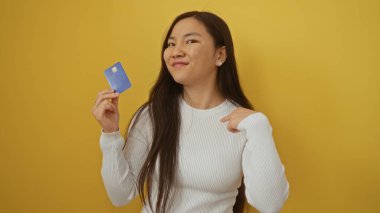 Kadın kendini gösterirken aynı zamanda kredi kartını canlı sarı arka planda tutuyor, kendine güvenini ve modern yaşam tarzını gösteriyor.
