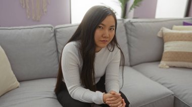 Modern bir oturma odasında rahat bir koltukta oturan bir kadın. Yumuşak ışıklandırmalı, sakin ve içsel bir titreşim yayıyor..