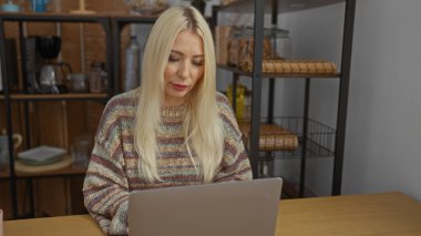 Dizüstü bilgisayarda çalışan, iç kısımları sarı saçlı, süveter giyen, raflarla çevrili ve oturma odası düzeninde ev eşyaları olan bir kadın, sıcak bir atmosferi çağrıştırıyor..