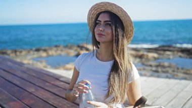 Bir kadın, deniz kenarında, açık havada güzellik ve rahatlık göstererek şişeyle gezmekten zevk alıyor..