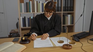Avukatlık bürosunda çalışan kadın yargıç, mahkeme salonundaki yasal düzenlemeler ve terazilerle ilgili notlar yazıyor.