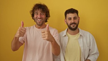 Gülümseyen ve başparmak kaldıran erkekler parlak sarı bir arka plana karşı poz veriyorlar, dostluk, mutluluk ve pozitif aile ilişkileri öneriyorlar..