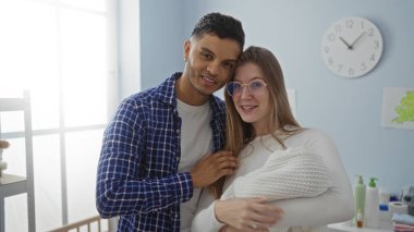 Kadın ve erkek rahat bir yatak odasında duruyor, yeni doğmuş bebeklerini sevgiyle kucaklıyor, huzurlu bir evde aile ve birlikteliği sembolize ediyorlar..