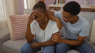 Anne ve oğul, sıcak bir oturma odasındaki kanepede birbirlerini rahatlatıyorlar. Aile ortamında sevgi ve destek gösteriyorlar..