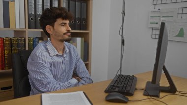 Ofis masasında çalışan sakallı yakışıklı genç adam profesyonel iş yerinde bilgisayarla çalışıyor. Kitaplar ve düzenli alan ayarları.