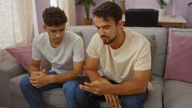 İspanyol erkekler rahat bir oturma odasında oturup, akıllı bir telefona odaklanıyorlar, aile sevgisini ve bağlantısını bir evde resmediyorlar..