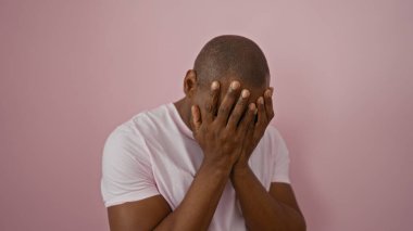 Pembe duvarın önünde yüzünü kapatan genç adam, izole edilmiş arka plan, duygular ve içgözlem görüntülerini basit bir ortamda yakalıyor. Kişiye ve canlı arkaplana odaklanıyor..