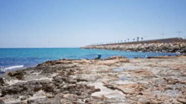 Mavi gökyüzünün altında turkuaz berrak suyla kayalık kıyı şeridinin odaksız görüntüsü