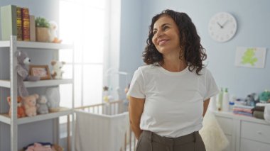 Bebek odasında beşikte oyuncaklarla ve dekorla çevrili bir şekilde gülümseyen bir kadın sıcak bir aile atmosferi yaratıyor. Huzurlu bir ortamda sıcaklığı ve şefkati yakalıyor..