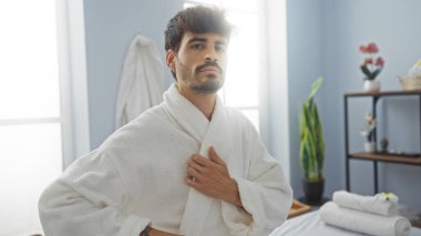 Kaplıcada sakallı, beyaz bornoz giyen, kendine güvenen, kendine güvenen genç bir İspanyol.