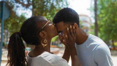 Şehir parkında sevgi dolu bir anda oğlunu alnından öpen bir kadın. Çevresi yeşillik ve şehir binalarıyla çevrili. Aile sevgisini ve birlikteliğini gösteriyor..