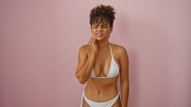 İzole edilmiş pembe arka planda bikinili bir kadın diş ağrısı çekiyor.