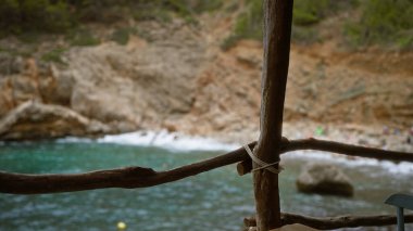 Cala Deia, Mallorca 'dan sahil manzarası, turkuaz sulara karşı kırsal ahşap korkuluklar ve açık havada serinleten engebeli uçurumlar..