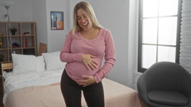 Hamile kadın içeride gülümsüyor, rahat yatak odasında karnına dokunuyor doğal ışık ve modern dekorla, sıcaklığını ve beklentilerini iletiyor..