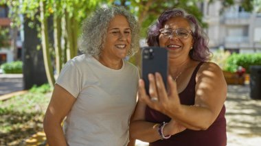 Dışarıda gülümseyen yaşlı kadınlar güneşli bir günde selfie çekiyorlar..
