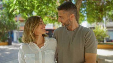 Açık havada gülümseyen bir çift, şehir merkezinde güneşli bir günde bir kadın ve bir erkek birbirlerine sevgiyle bakar.