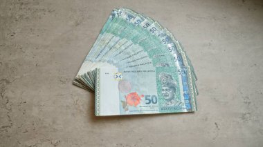 Beton bir yüzeye yerleştirilmiş Malezya banknotları, bir hayran düzeninde 50 ringgit banknotunu gösteriyor, Malezya ve finans temalarının yerel para birimlerini vurguluyor.