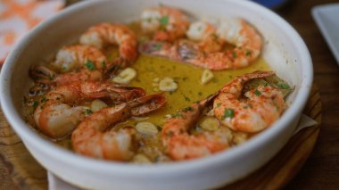 Close-up showcasing a delicious shrimp dish served in a white bowl with garlic and herbs, evoking flavors of seafood dining in a restaurant setting clipart