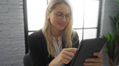 Modern ofiste çalışan, gözlük takan, tablet sarışını iş kadını gülümseyen, profesyonel, beyaz iş kadını odaklı bir kadın..