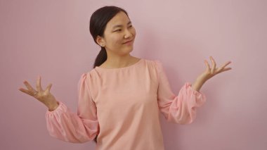 Pembe bluz giyen bir kadın, izole edilmiş pembe arka planda kendine güvenerek duruyor. Zarafet ve güzellik sergiliyor..