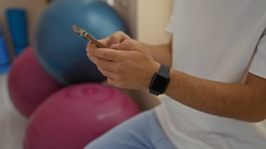 Akıllı adam spor salonunda akıllı telefon kullanıyor. Arka planda egzersiz topları var. Teknoloji ve sağlık odaklı modern fitness yaşam tarzını içeride gösteriyor..