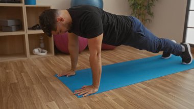 Adam spor salonundaki mavi paspasın üzerinde ahşap zemin ile şınav çekiyor. Sağlıklı bir yaşam tarzı için spor salonunda spor yapıyor..