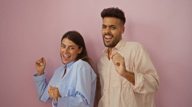 Pembe bir duvarın karşısında neşeyle dans eden erkek ve kadın, canlı ve izole bir ortamda mutluluk ve birlikteliği ifade ediyor..