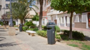 Ağaçların, yeşil bitkilerin ve kentsel binaların olduğu bulanık bir açık hava sahnesi. Parlak ve güneşli bir gün.