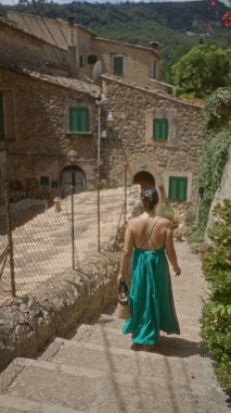 Mallorca 'da Valldemossa' nın tarihi sokaklarında yürüyen, yeşil bir elbise giyen ve elinde sepet tutan bir kadın İspanya 'da bir yaz gününün özünü yakalıyor..