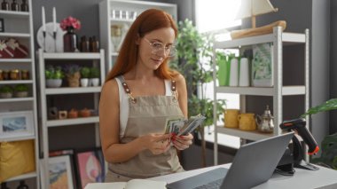 Kızıl saçlı genç bir kadın bir dekor dükkanında para sayıyor. Etrafı fabrikalar ve raflar da dahil olmak üzere dekorasyon malzemeleriyle çevrili. Bu da kapalı bir yerde perakende şirketi kurulduğunu gösteriyor..