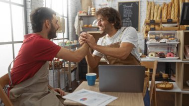 Fırındaki adamlar ellerinde laptopla masada el sıkışıyorlar, etrafı pişmiş mallarla çevrili, parlak, endüstriyel temalı bir iç mekanda takım çalışması öneriyorlar..