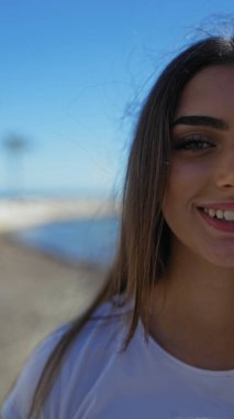 Arka planda açık mavi gökyüzü ve okyanusla deniz kenarında gülümseyen bir kadın canlı, açık hava atmosferini yakalıyor..