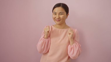 Pembe bluzlu genç Çinli bir kadın, pembe bir arka plana karşı güvenle gülümsüyor, iyimserlik ve çekicilik duygusu sergiliyor..