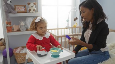 Sıcak yatak odasında kızıyla etkileşime giren bir kadın aile sevgisini ve bağlantısını oyuncaklarla ve sıcak bir ev ortamını gösteren bir beşikle sergiliyor..